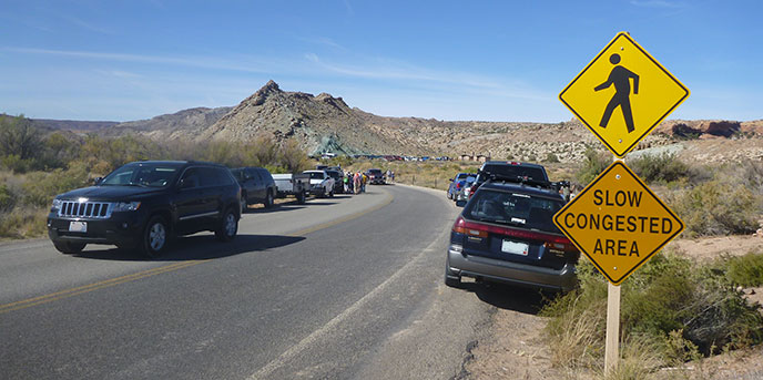 A road sign reading "slow congested area" with cars parked on the shoulder.