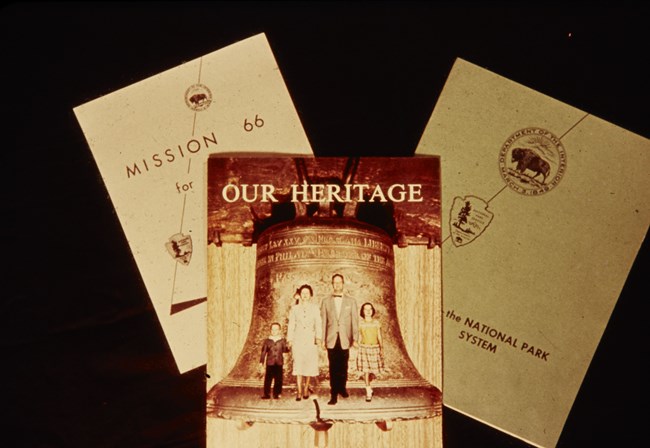 Three brochures are laid flat on a table, titled "Our Heritage", "Mission 66", and one illegible title