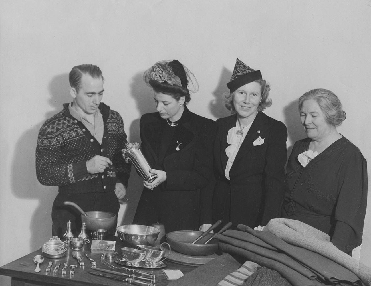 A man and three women stand behind a table displaying petwer and woolen cloth.