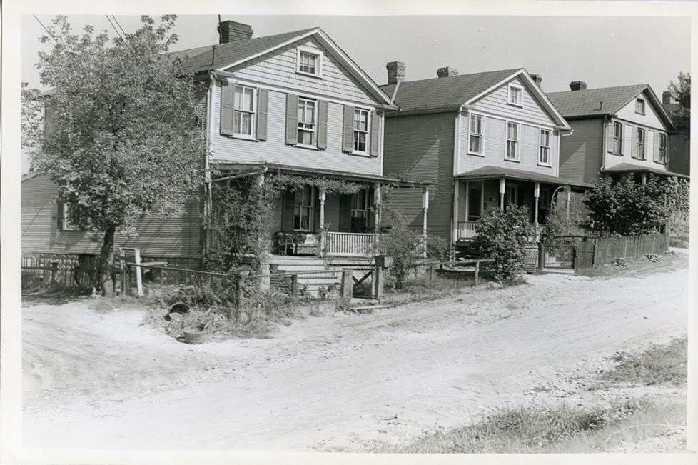 Black and white photo of three wood frame houses. Each has a porch and three windows on the second floor front.