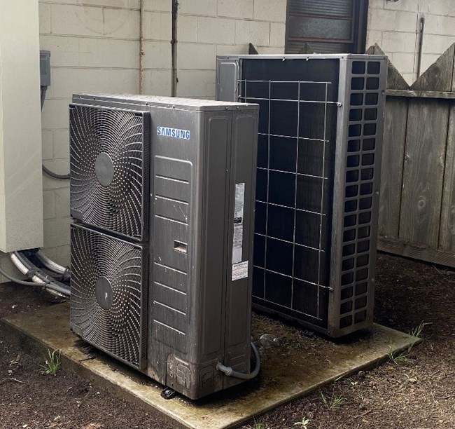 Two heat pumps sit on a pad outside a building at Fort Funston