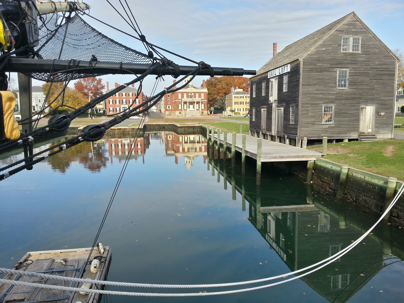 Historic buildings made of brick and wood surround a wharf with the water reflecting their image.