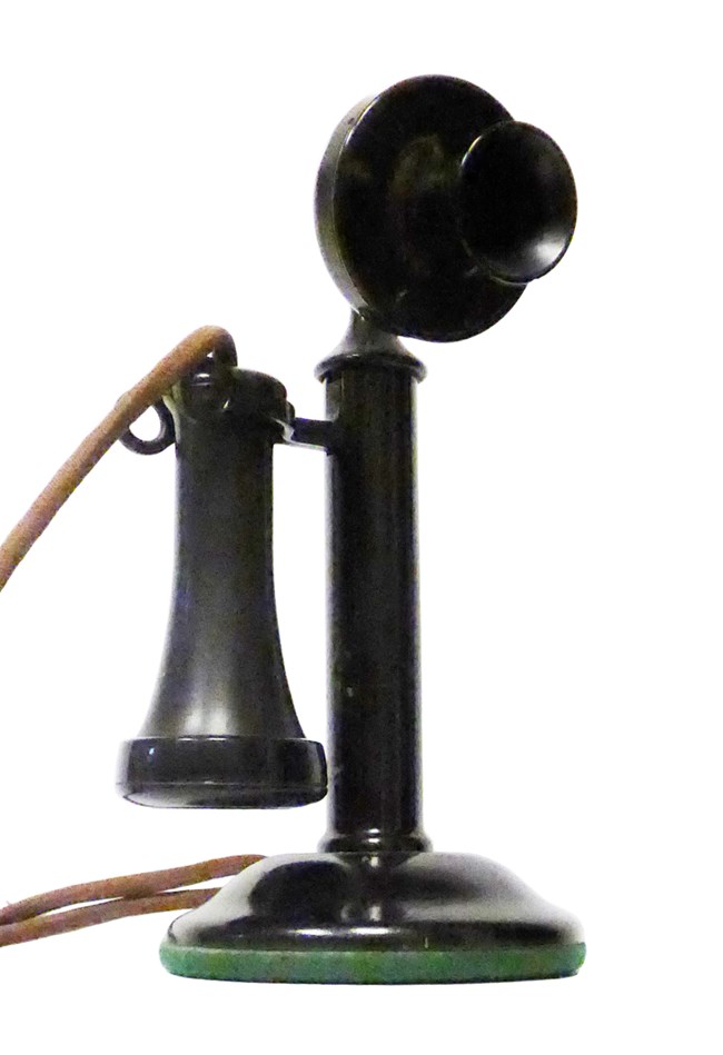 black telephone with round mouthpiece on stick and cone shaped earpiece with cord on stand