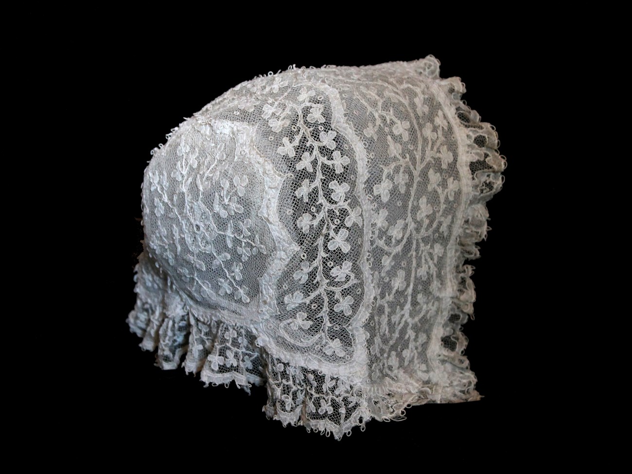 A white lace baby bonnet decorated with shamrocks