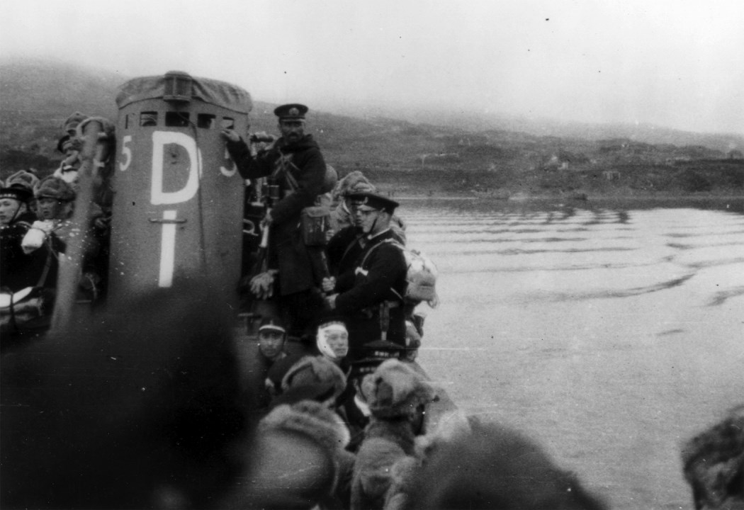 Men crowd onto a submarine with water in the background.