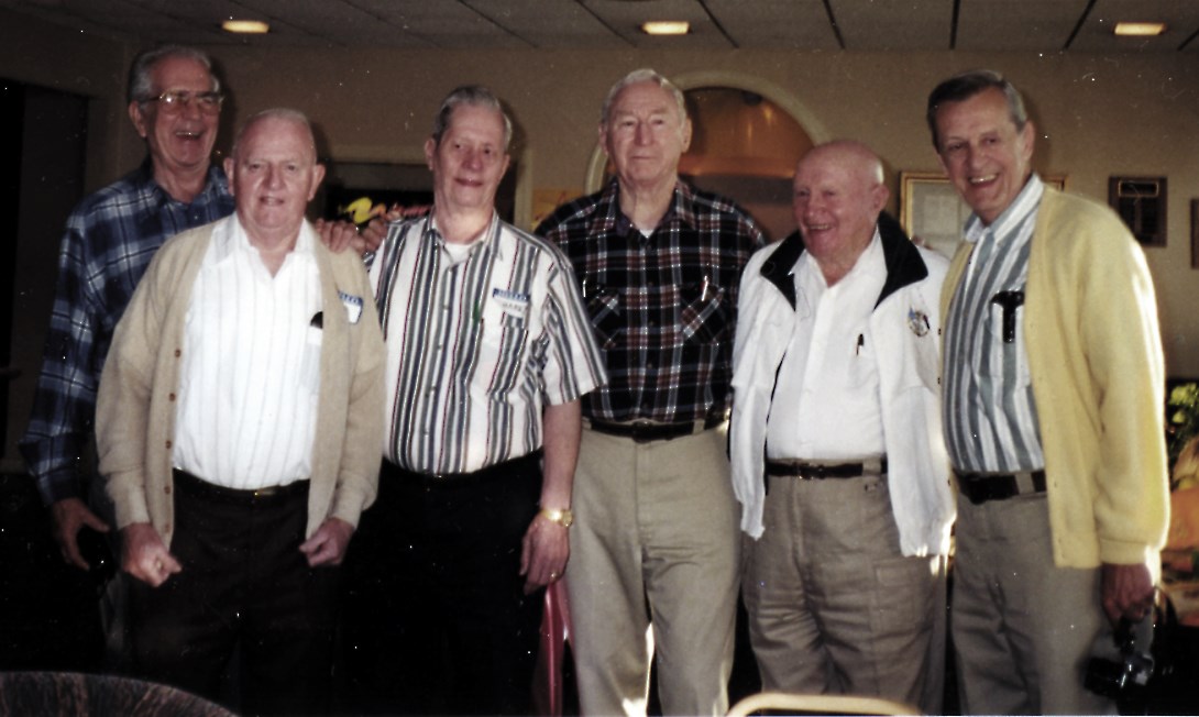 Older men with gray or white hair standing inside a hall.