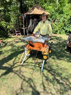 A man in a straw hat standing behind a table saw.