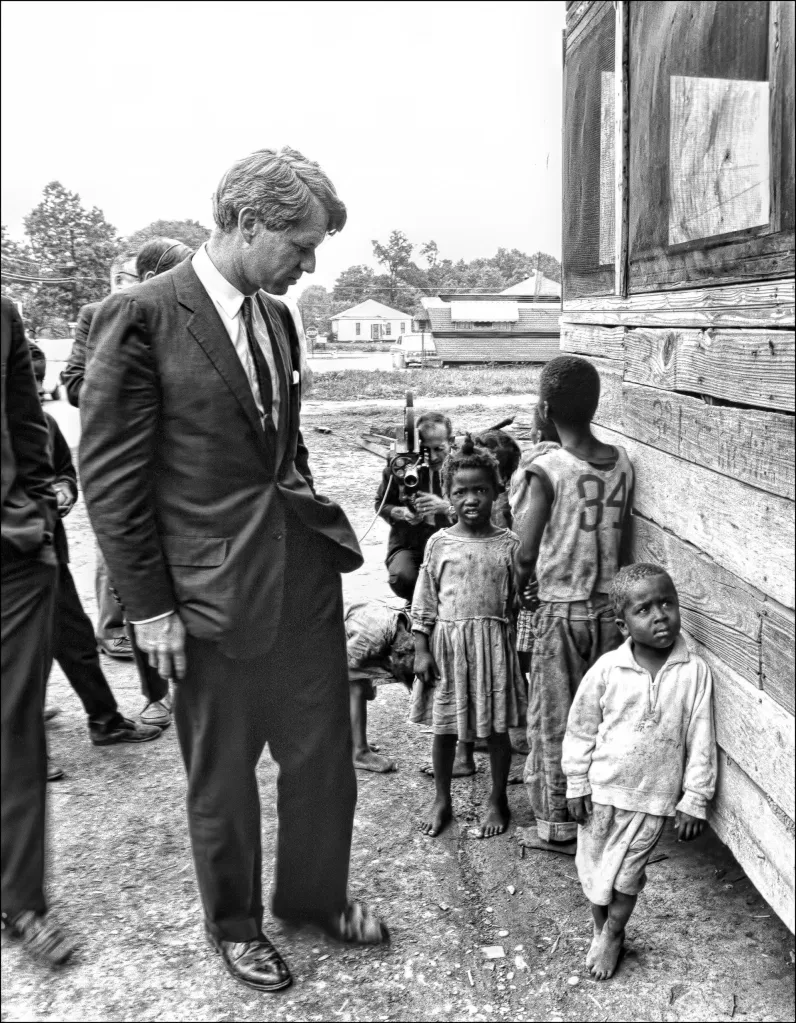 A black and white photo of RFK on the left.  Several children are gathered on his right.