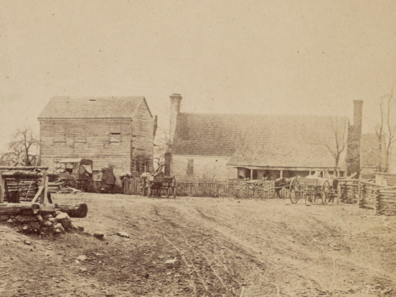 Simple wooden clapboard building with porch and two chimneys in muddy carriage yard