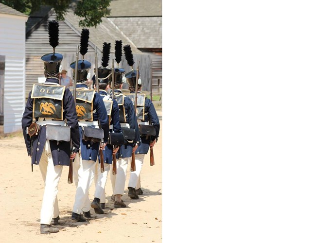 Line of five people, each wearing blue military style uniforms with a golden eagle and the letters OLI on their back.