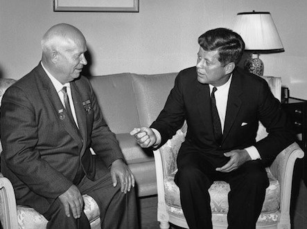 The two men are seated in chairs.  Khrushchev is on the left and Kennedy is on the right.  A couch and lamp are behind them.