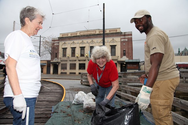 Olf smiling with two other ladies while picking up trash by some train tracks