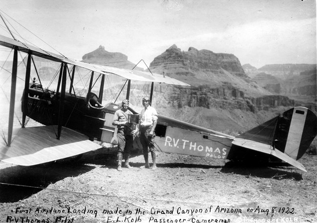 Two pilots standing next to a biplane.