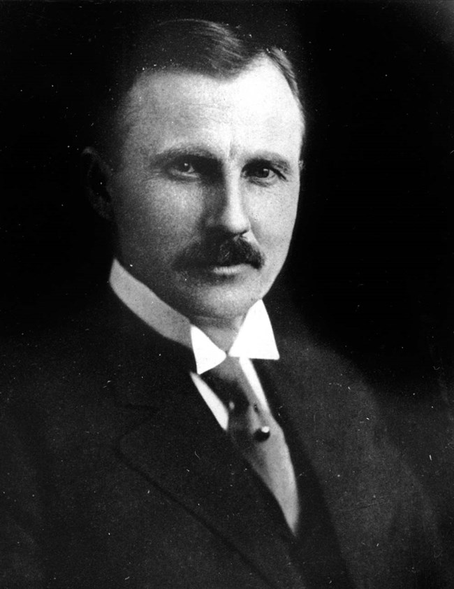 Bust-up portrait of a man in a dark suit and mustache.