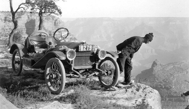 Driver stands next to his car and peers over the edge of the canyon.