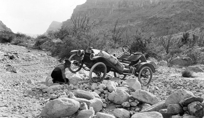 Metz on a section of rocky ground, with driver inspecting a wheel that is tilted up.