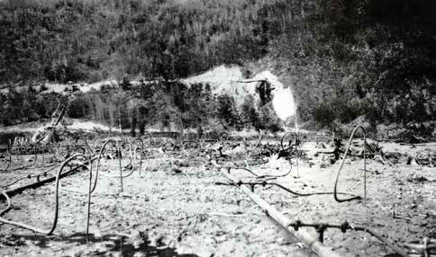 pipes sticking into mud in front of a hilly forest