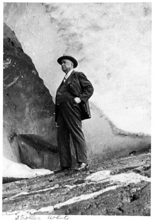 An older man in a suit stands upon a glacier.