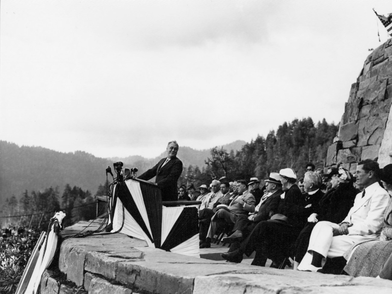 A man at a podium (FDR) speaks to a crowd in a mountainous landscape.