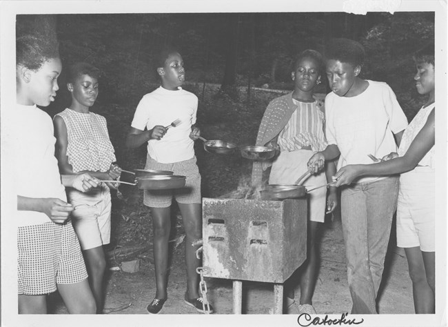 Youth cook with skillets on an outdoor grill.
