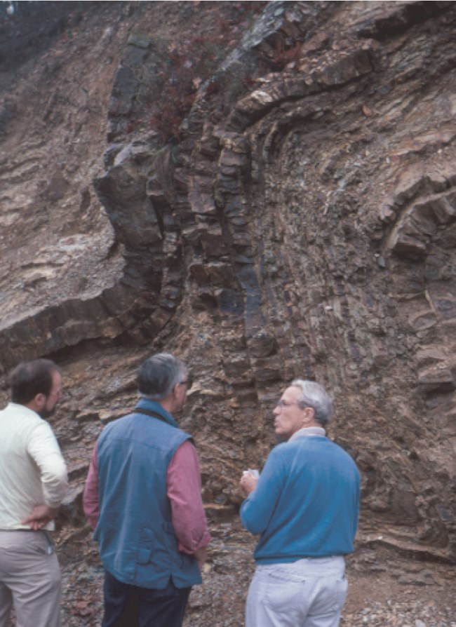 three people standing in front of rock cliff with folded rock layers