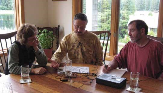 Three people sit at a table with audio recording equipment.