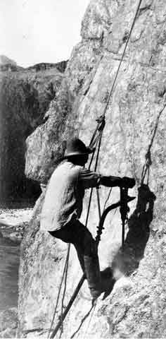 Man in a rope harness suspended against a cliff face.