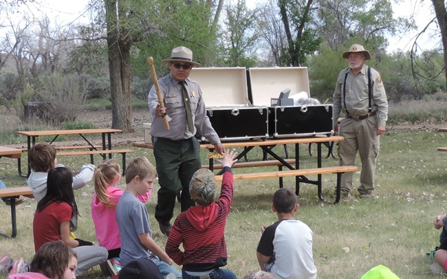 Two rangers showcasing a travel trunk to students.