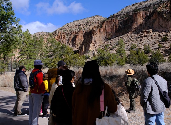 A large group of visitors stand around a park ranger as she talks about the canyon in front of them.