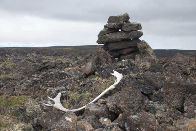 A caribou antler sits in front of a stone structure, with cloudy skies in the background
