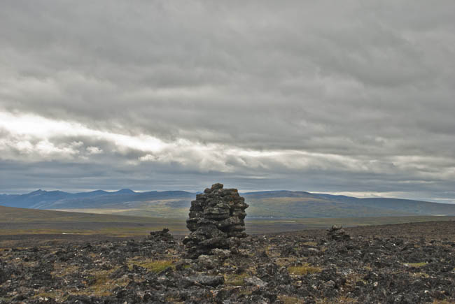 Stormy skies boil dramatically behind ancient stone structures on the caldera rim