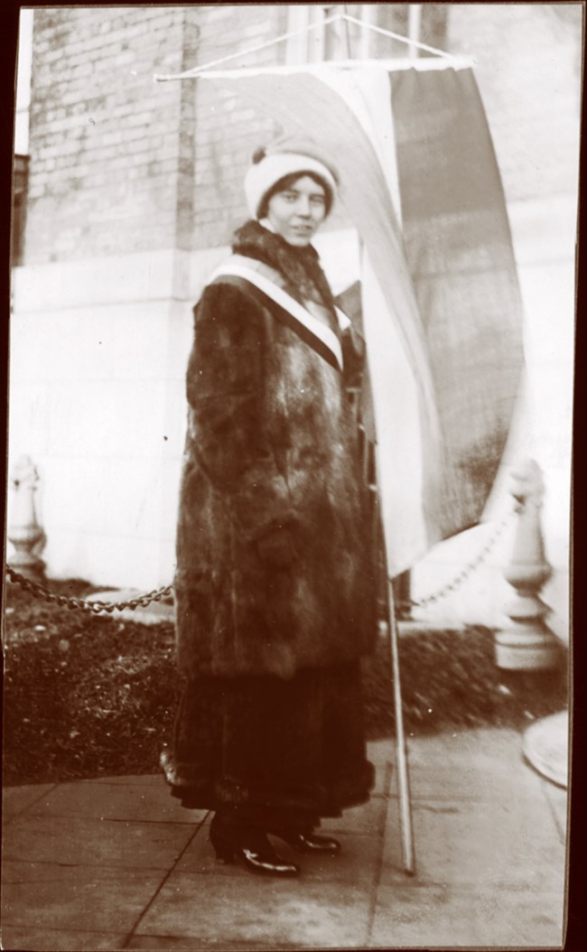 Alice Paul outside holding a tri-colored suffrage banner