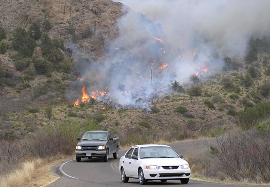 Cars drive down to the Basin Campground as the fire burns in the background
