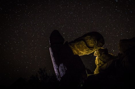 A yellow light dimly illuminated large rocks, with the night sky highlighted in the background.