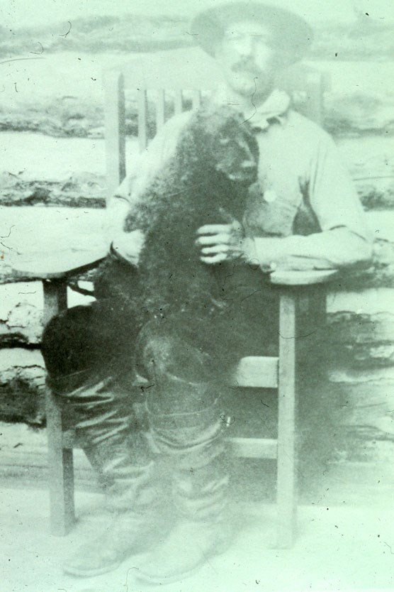 Doc Barry sitting on the porch in a rocking chair with a black dog on his lap.