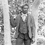 Israel Lafayaette Jones as a young man dressed in a suit leaning against a tree.