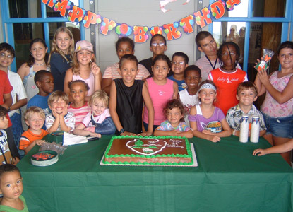 Smiling children surround a birthday cake featuring the National Park Service arrowhead symbol.
