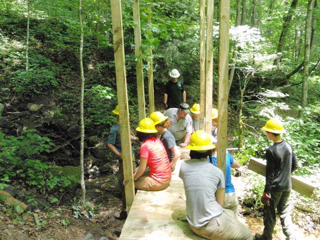 A group of young adults working together to rebuild a bridge on a trail