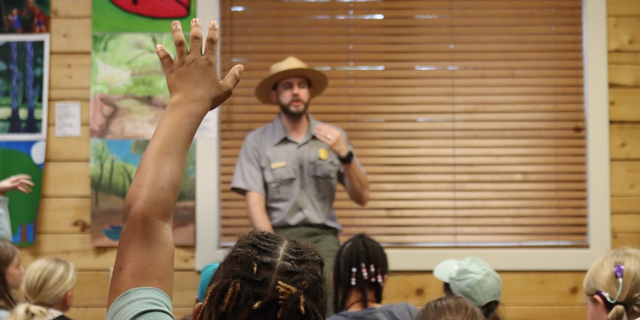 A child seated on the Visitor Center floor raises their hand during a field trip.