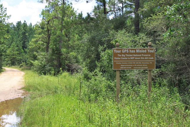 Brown sign among green bushes reads, "Your GPS has Misled You! The Big Thicket National Preserve Visitor Center is not down this dirt road."
