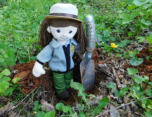 A rag doll dressed like a female park ranger stands beside a hole in the ground