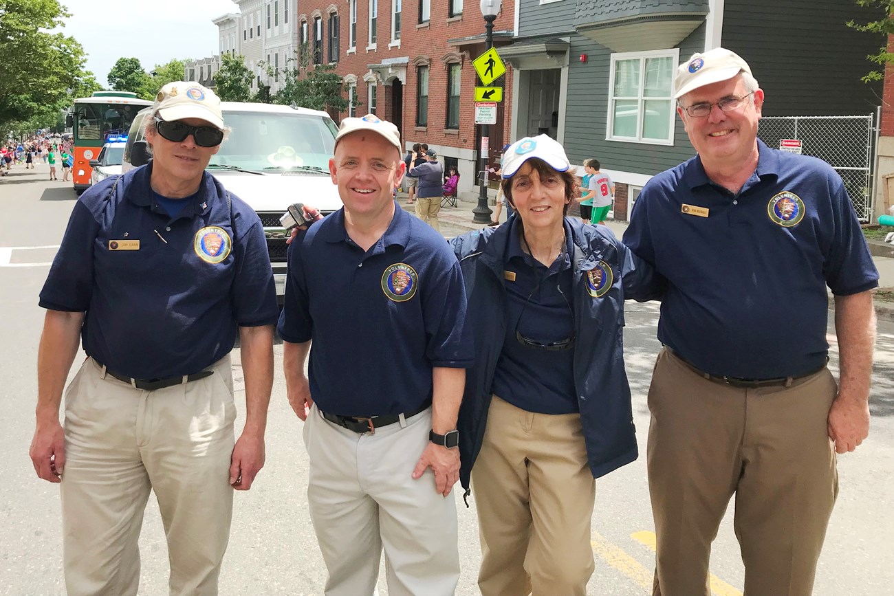 four middle-aged people wearing hats and navy blue polos smiling at the camera