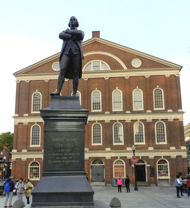 A bronze statue in front of the red brick Faneuil Hall.
