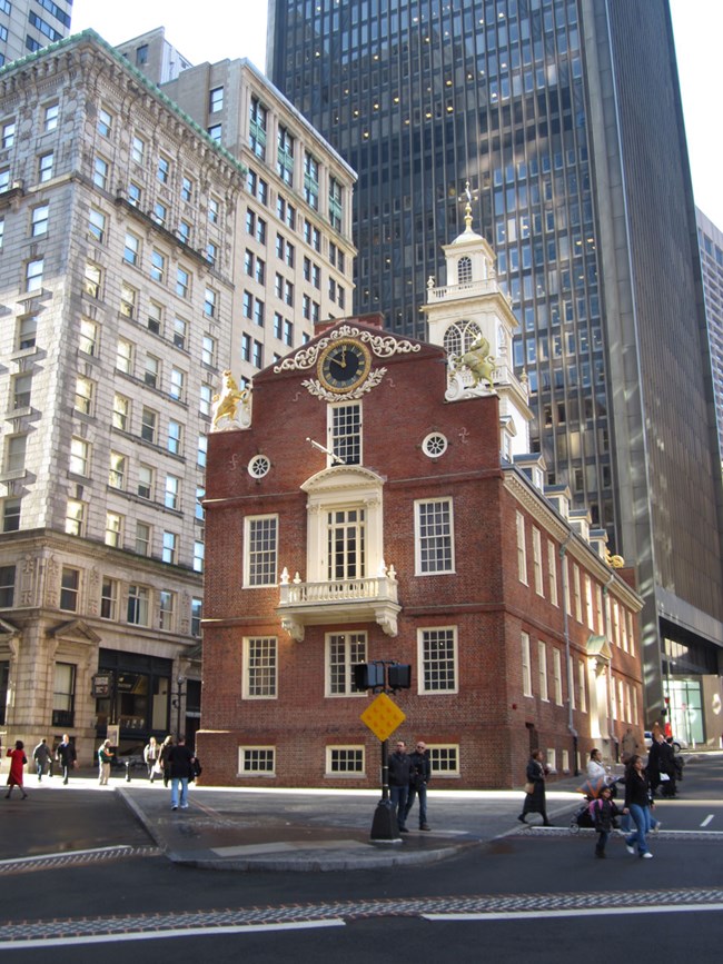 Old State House is a two story brick structure that features a second floor balcony overlooking a main intersection of the city. A clock is above the balcony and a cupola adorns the top of the building at the center.