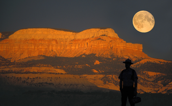 Dark Ranger Silhoutte with full moon rising over plateau with alpine glow.
