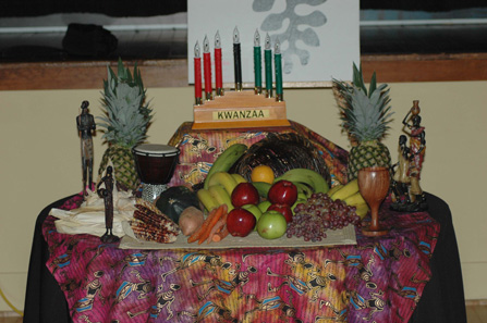 A table with fruit, vegetables, African figurines, and kinara with candles for a Kwanzaa celebration.