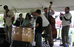 Carlos Martinez and three students play the drums while displaced New Orleans jazz musicians play their instruments in the background.