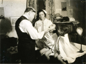 Two African American children being examined by a doctor with a nurse standing nearby.