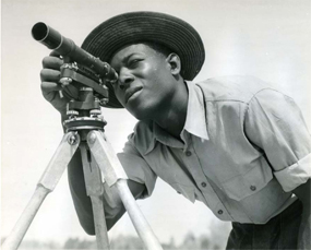 African American man looking through a surveyor's scope.
