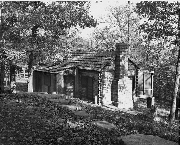 black and white photo of wooden cabin with stone chimney and screened porch